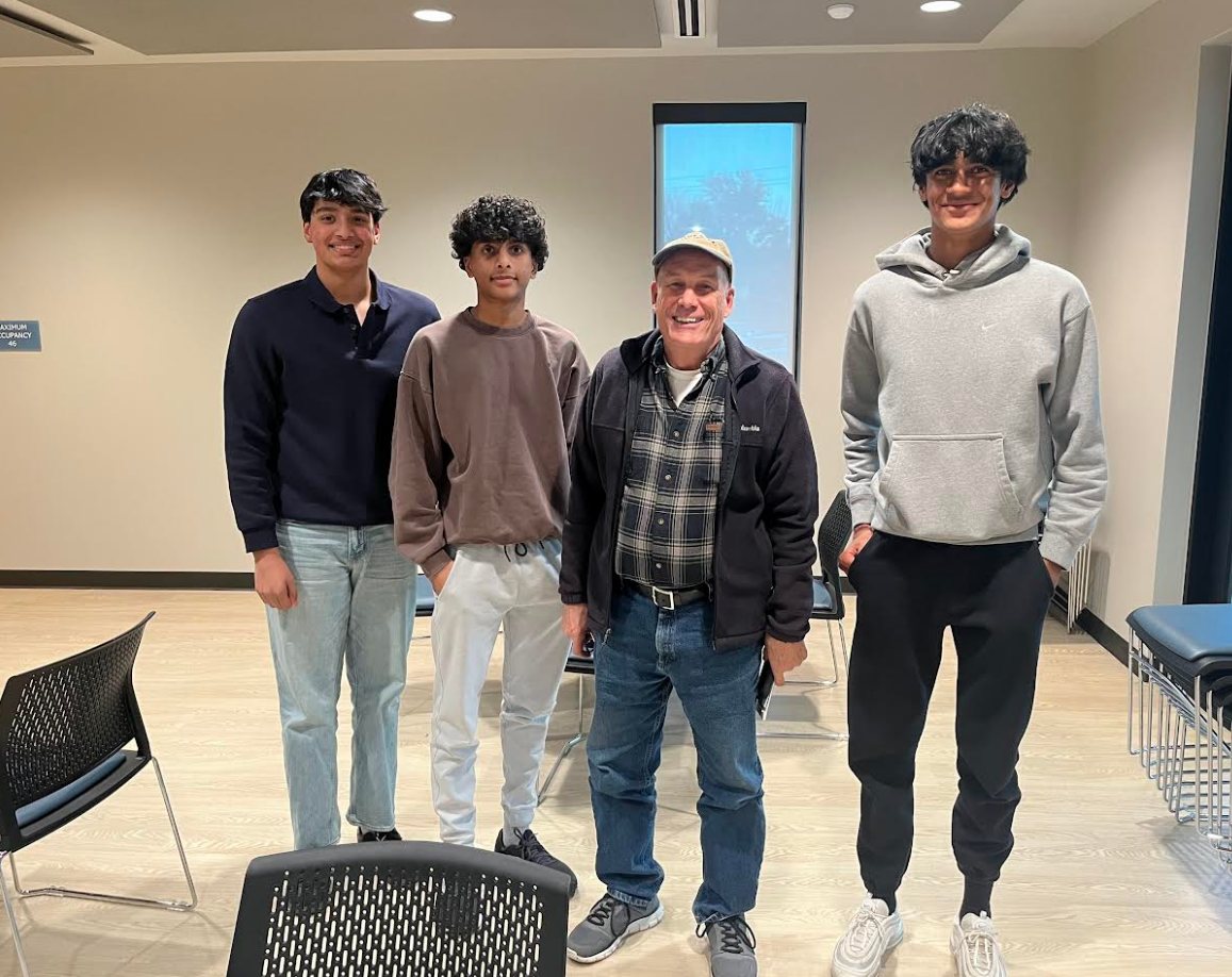 Three ElderTech students standing with a smiling older man in a community room