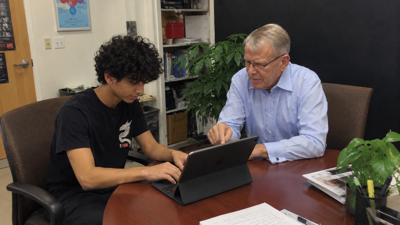 A student working through a tablet with an older man who is pointing at the screen
