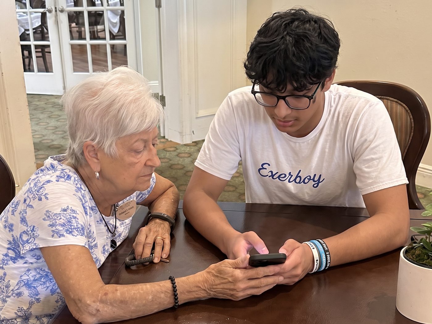 An ElderTech volunteer helping an older woman with her smartphone at a senior community table